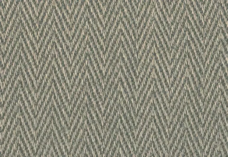 Close-up of a woven fabric with a herringbone pattern in shades of beige and gray. The texture shows tightly interlaced fibers forming a diagonal zigzag design.