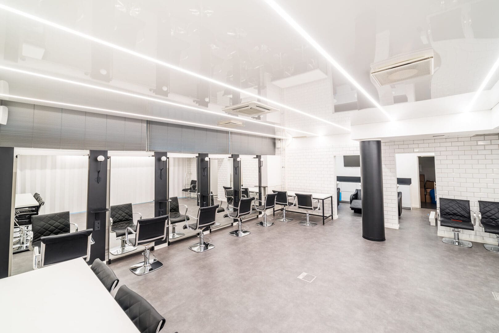 A modern, well-lit hair salon with multiple styling stations, black chairs, mirrors, and white walls, featuring a minimalist design.