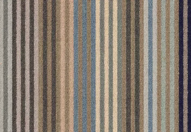 A close-up of Margo Selby Stripe Surf with alternating vertical bands in various colors, including shades of grey, blue, beige, and brown. The texture appears to be woven or knitted.