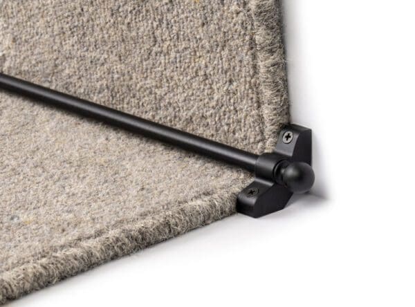 A close-up of Stair Rods - Jubilee with black brackets installed on a grey carpeted step, securing the carpet in place.