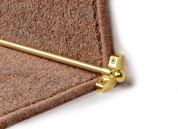 A close-up of a Stair Rods - Jubilee securing a brown carpet runner on a staircase.