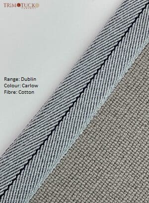 A close-up of a fabric sample labeled "Range: Dublin, Colour: Carlow, Fibre: Cotton" from Dublin Binding, showing a light blue herringbone pattern beside a textured beige material.