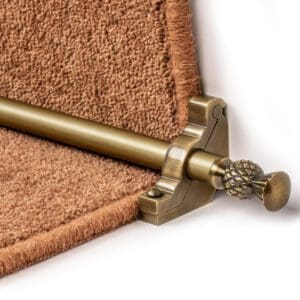 Close-up of Stair Rods - Country Arran secured by an ornate bracket on a brown carpeted step.