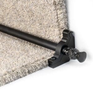 A black metal stair rod with decorative finials secures gray carpet on a staircase.