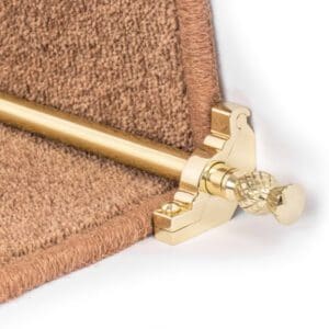 Close-up of a brass stair rod and bracket securing the edge of a brown carpet on a staircase.