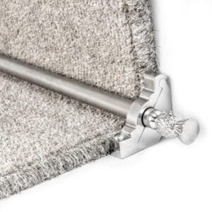 Close-up image of a carpet stair rod secured by a decorative bracket at the corner of a carpeted step.