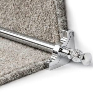 Close-up of a silver stair rod with a decorative end cap, installed over light grey carpet on a staircase.