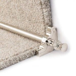 Image of a metal stair rod secured at the base of a carpeted stair, holding the carpet runner in place.