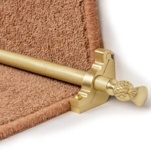 A brass stair rod with an ornamental finial is installed at the edge of a carpeted stair.