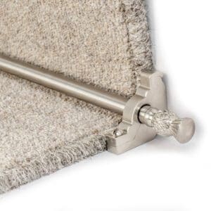 Close-up of a gray stair carpet with a silver stair rod and finial, used to hold the carpet in place. The rod is securely fitted into brackets on either side of the stair.