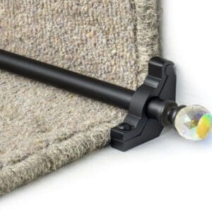 Close-up of a black stair rod with a decorative crystal finial securing a beige carpet on a staircase.