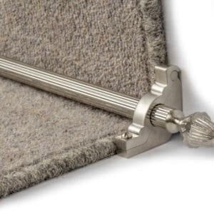 A close-up of a stair rod secured with a decorative metal finial, holding a carpet runner in place on a stair.