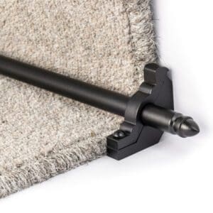 A black stair rod installed on the edge of a step with beige carpet.