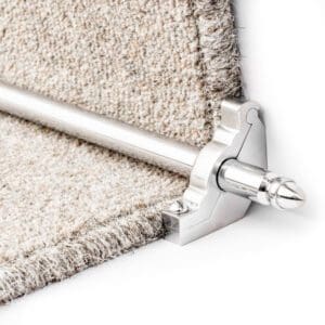 Close-up view of a brass stair rod and bracket securing a beige carpet on a staircase.