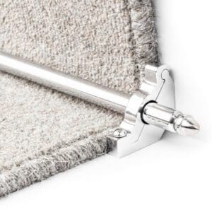 A close-up of a stair rod with a metallic bracket securing a beige carpet at the corner of a step.