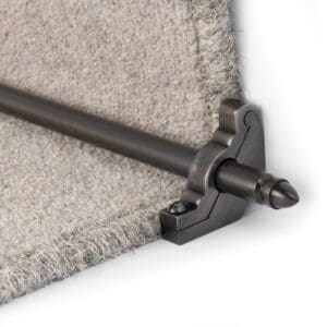 Stair rod securing the edge of a beige carpet on a step. The rod is held in place by a decorative bracket.