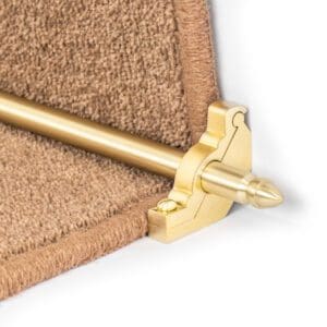 Close-up of a brass stair rod and bracket securing a brown carpet runner on a staircase.