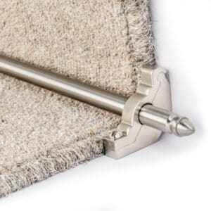 Close-up of a carpet with angled stitching secured by a metallic stair rod holder and rod at the corner.