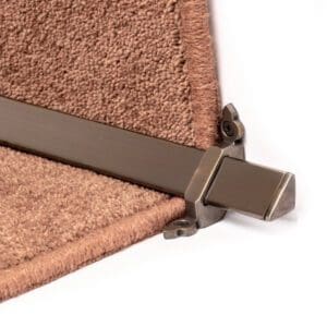 Close-up of a metal stair rod securing the edge of a brown carpeted stair.