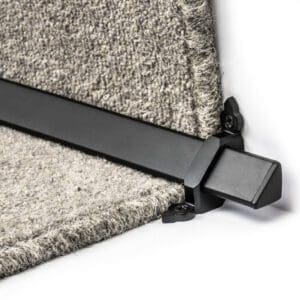 Close-up of a black metal bracket securing the edge of a piece of gray carpet.