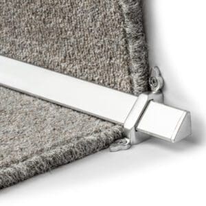 Close-up of a silver, metal stair rod securing two sections of a grey carpet on a staircase.