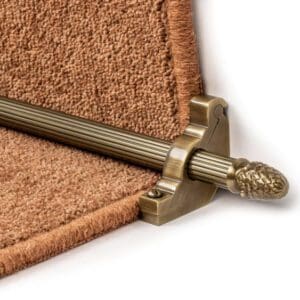 Close-up of a Stair Rods - Sherwood with a decorative end cap holding a brown carpet runner in place on a staircase.