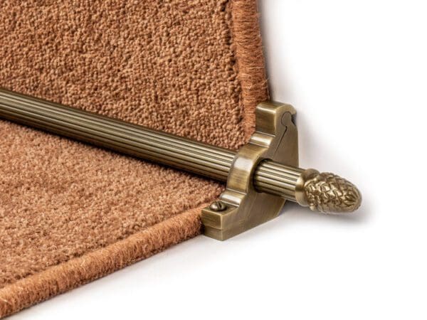 Close-up of a Stair Rods - Sherwood with a decorative end cap holding a brown carpet runner in place on a staircase.