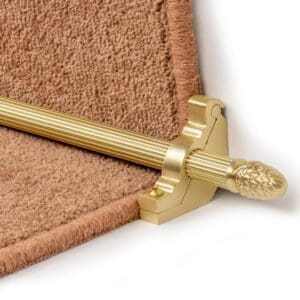 A close-up of a decorative gold stair rod bracket with a textured, brown carpet in the background.