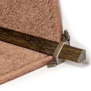 Close-up of a carpet runner bar held in place by a metal bracket at the edge of a carpeted staircase.