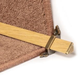 A close-up of a wooden Stair Rods - Tudor Light securing a beige carpet corner in place with screws visible in the metal bracket.