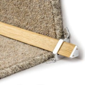 A close-up of a wooden stair rod with metal brackets securing it in place on a carpeted stair.