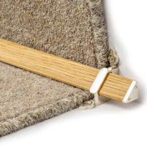 Close-up of a corner carpet gripper holding beige carpet with a wooden strip.