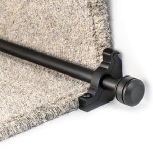 A black rod is installed at the edge of a stair step covered with beige carpet, secured in place by a black bracket.