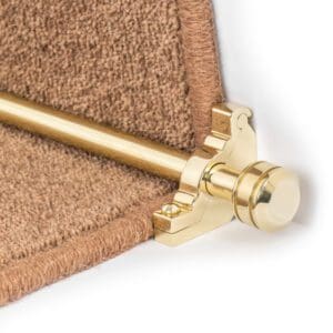 A close-up view of a gold carpet rod fixed on brown carpeted stairs.