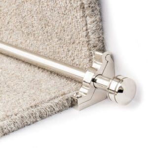 Close-up of a stair rod with a silver finial securing the edge of a beige carpet on a staircase.