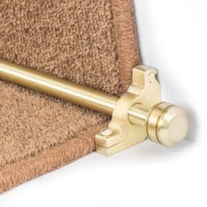 A close-up image of a brass stair rod and bracket installed on a brown carpeted stair.