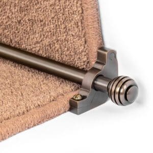 Close-up of a metal stair rod with decorative end caps securing a section of brown carpet on a staircase.