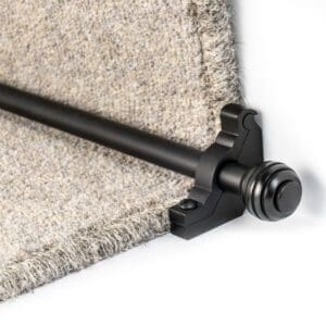 A metal stair rod with a decorative end cap is installed at the edge of a carpeted stair step.