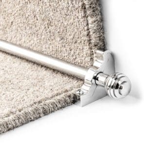 Close-up of a silver stair rod supporting the edge of a beige carpet stair runner.