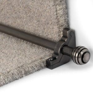 Close-up of a stair rod bracket holding a metal rod against a beige carpeted step.