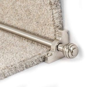 Close-up of a metal stair rod installed on a carpeted stair riser, showing the rod's end bracket and the textured edges of the carpet.