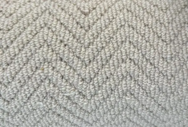 Close-up of a light grey fabric with a herringbone pattern. The surface has a soft, textured appearance with neatly arranged woven fibers, known as Wool Skein Herringbone Landes.